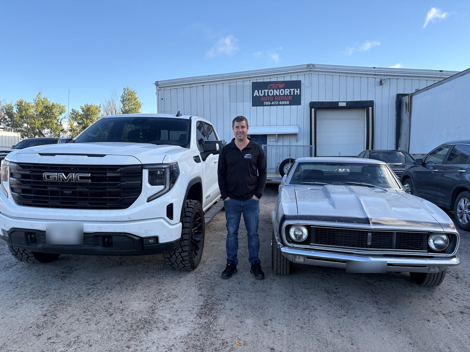 Ryan Christadler standing between a pickup truck and a classic car in front of the AutoNorth Auto Repair shop in North Bay