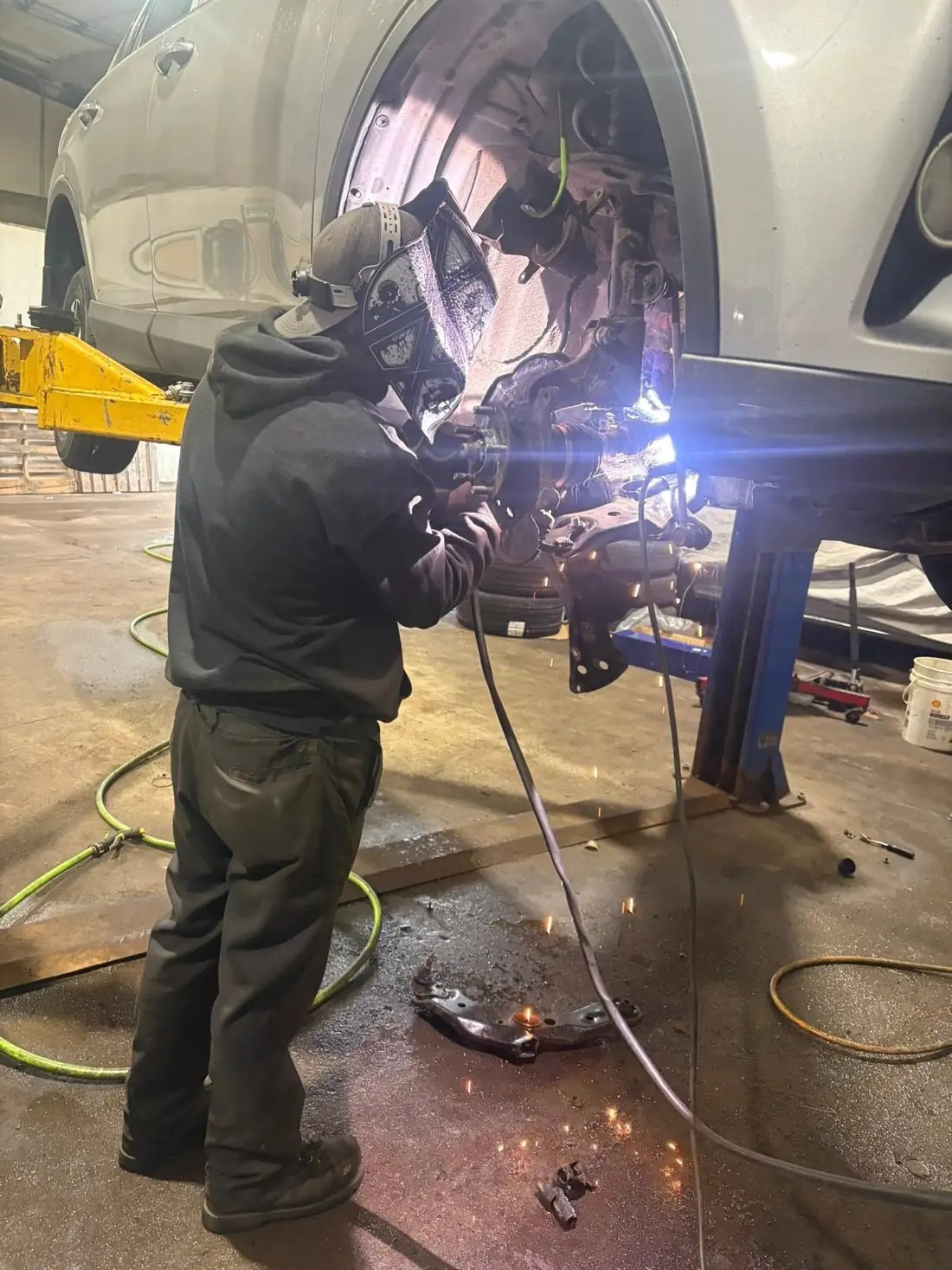 An AutoNorth technician welding a suspension repair under a car on a hoist