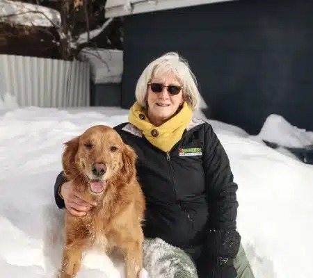 Lori Johnston of Bark Busters sitting in the snow with Finn, her blind golden retriever