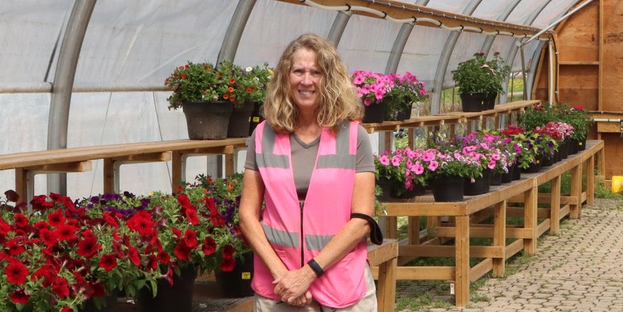 Benches of red and pink annuals inside a Laporte's Nursery greenhouse, with a staff member in a pink safety vest