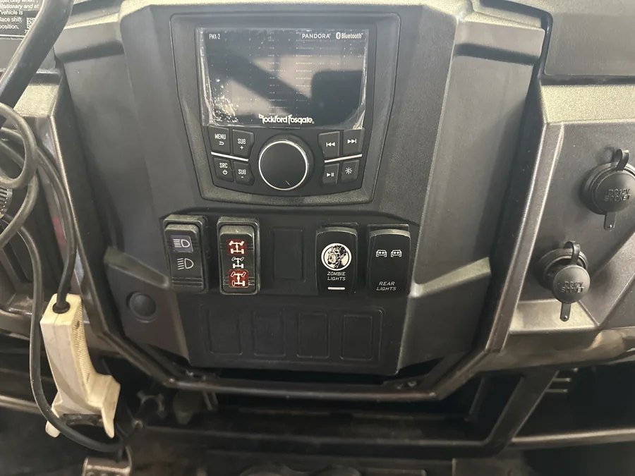 A UTV dash with a Rockford Fosgate head unit and a row of switches