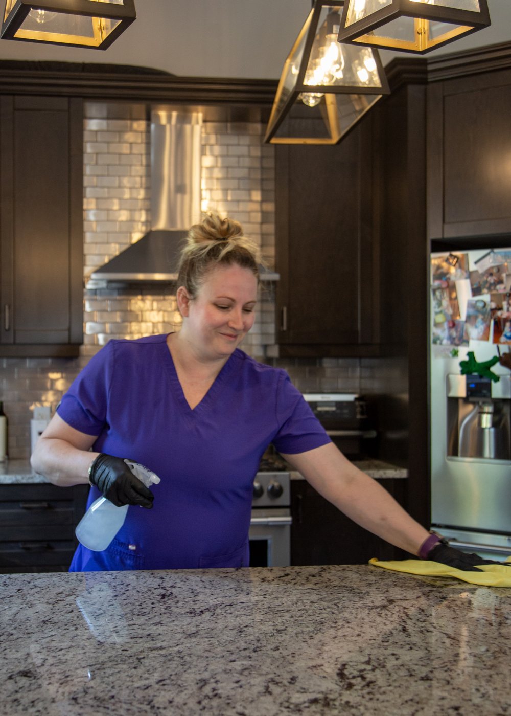 A Maid In The North cleaner in purple scrubs wiping down a granite kitchen island