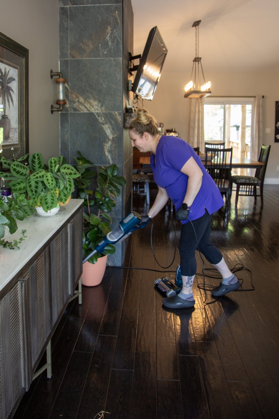 A Maid In The North cleaner vacuuming a dining room with dark hardwood floors