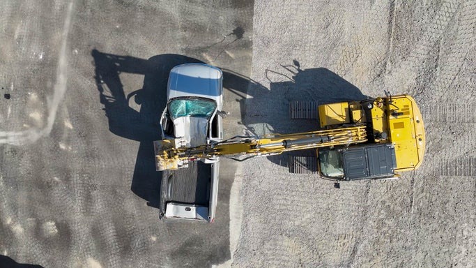 Overhead view of a MASHinery excavator crushing a pickup truck on the car smash pad north of North Bay