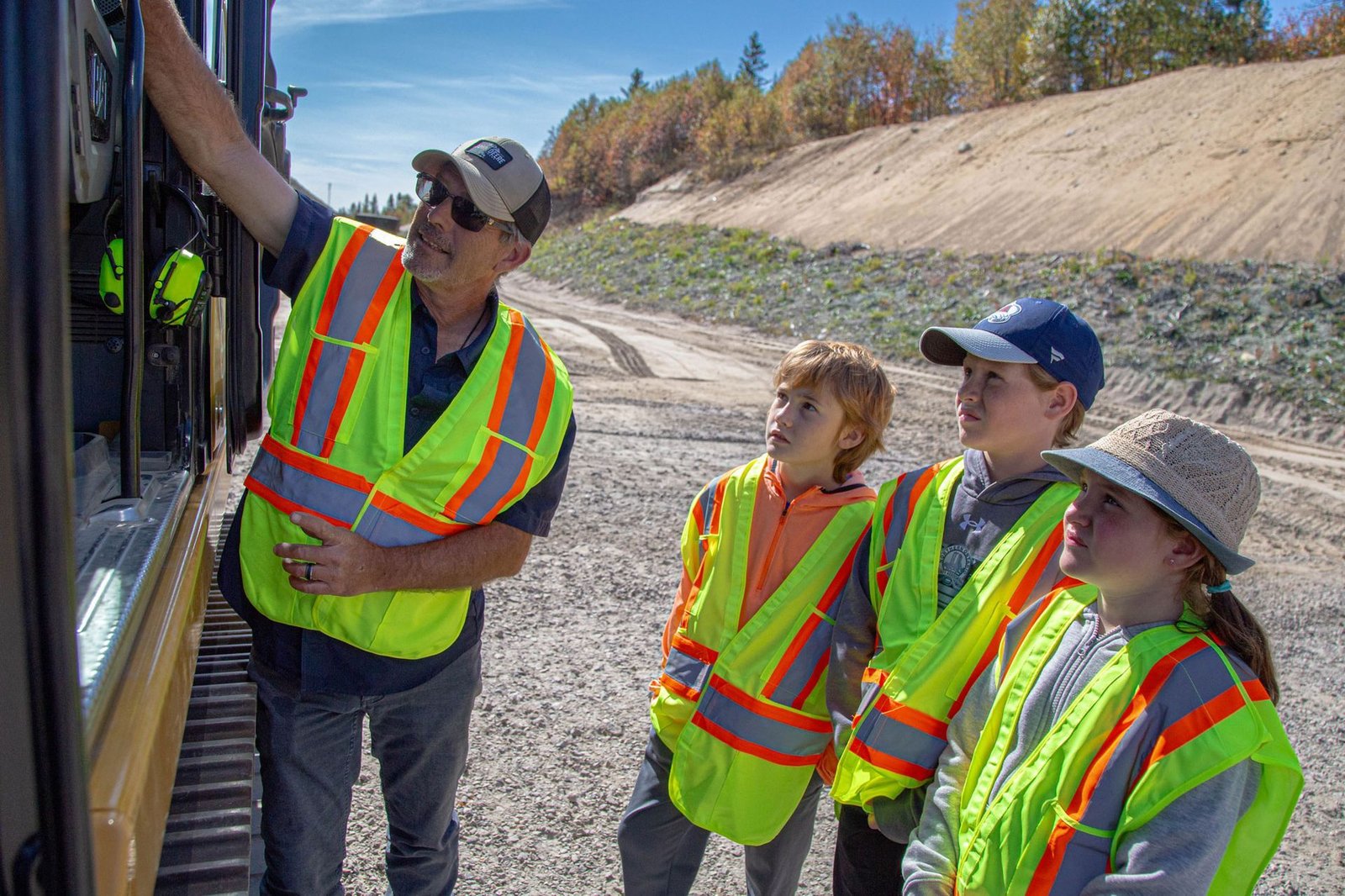 John Perry of MASHinery showing three kids in safety vests how an excavator works
