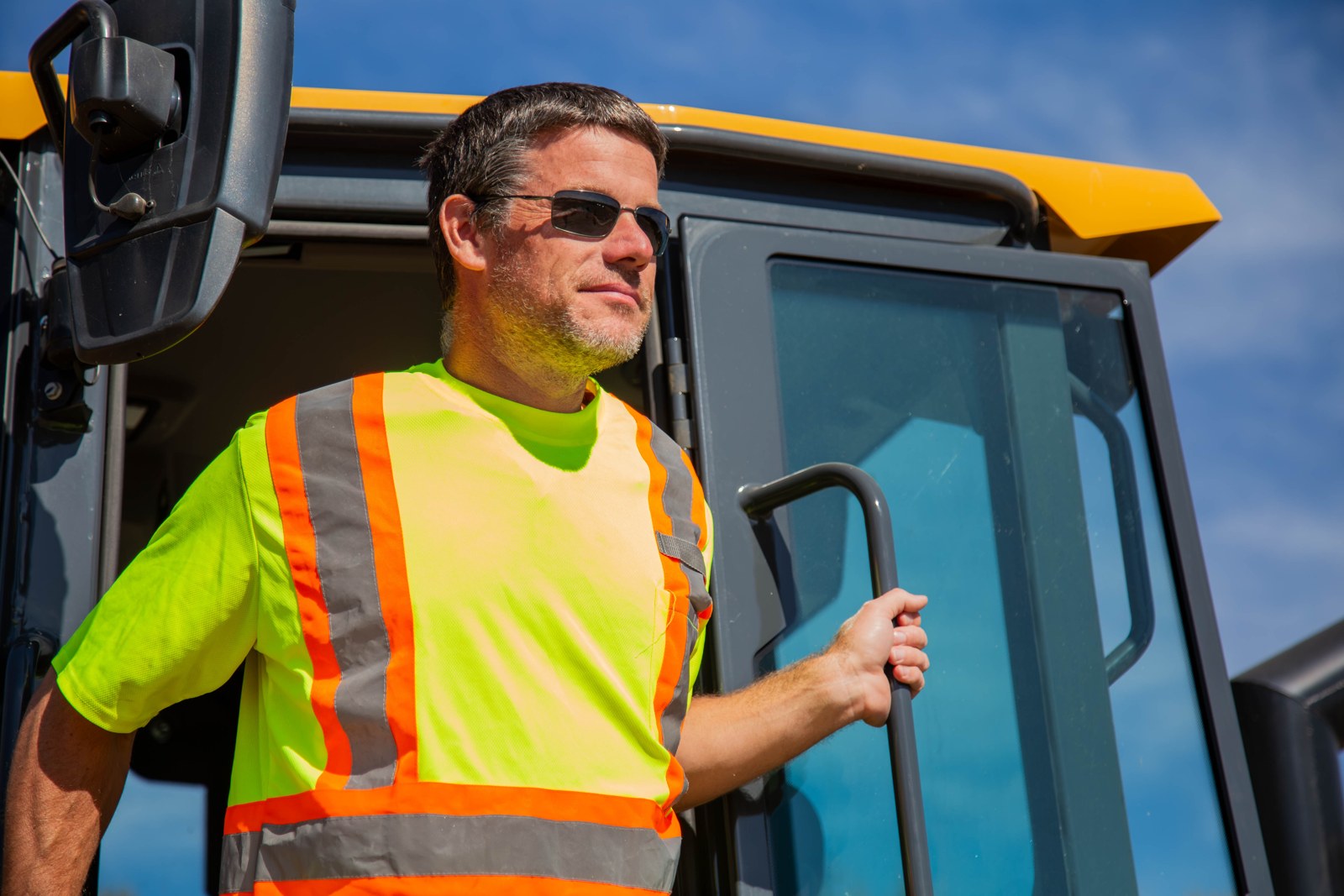 Ken Sim, founder of MASHinery, standing in the cab door of a yellow excavator