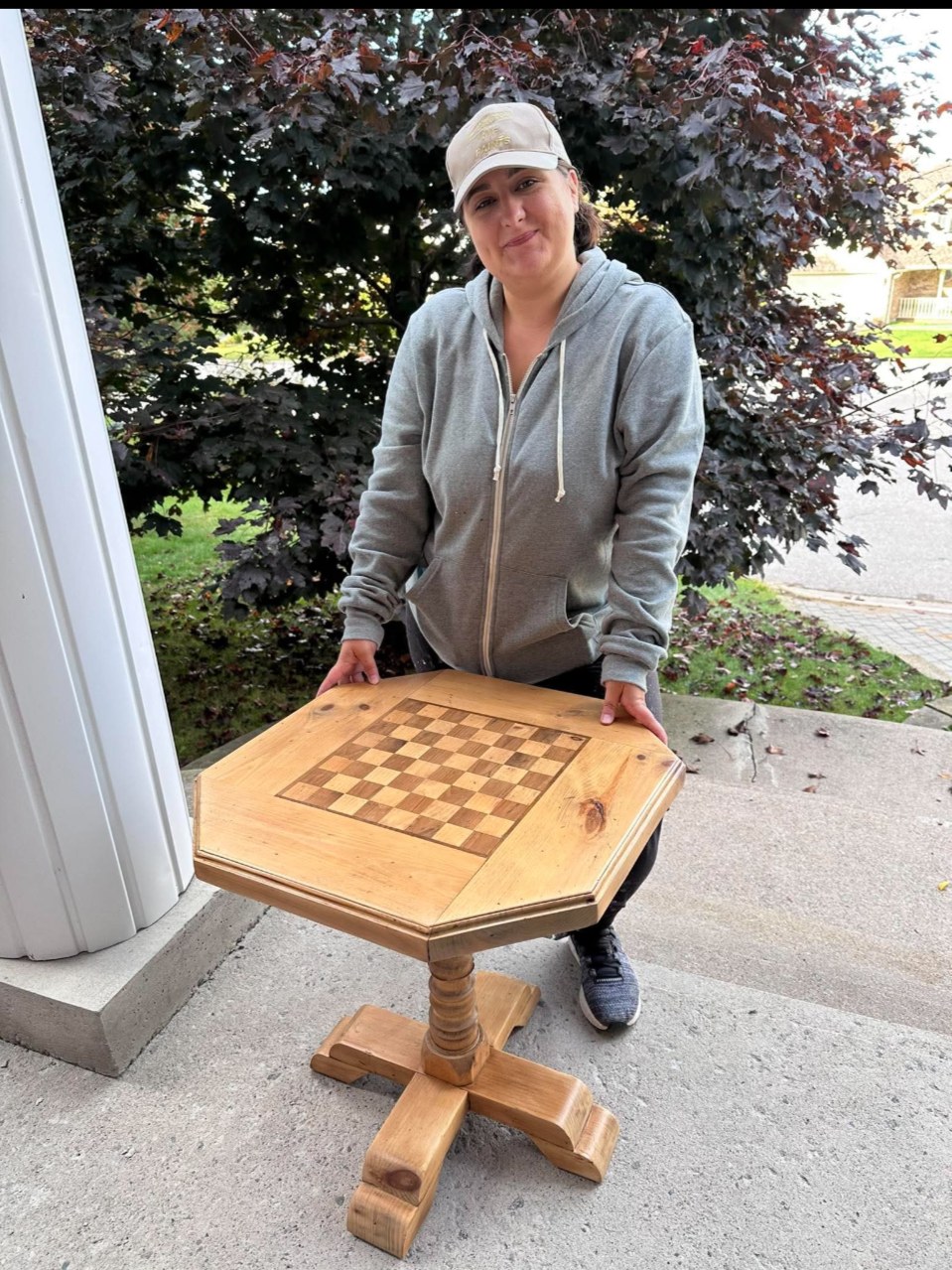 Cyan Goulet kneeling behind an octagonal pine chess table she refinished for a client
