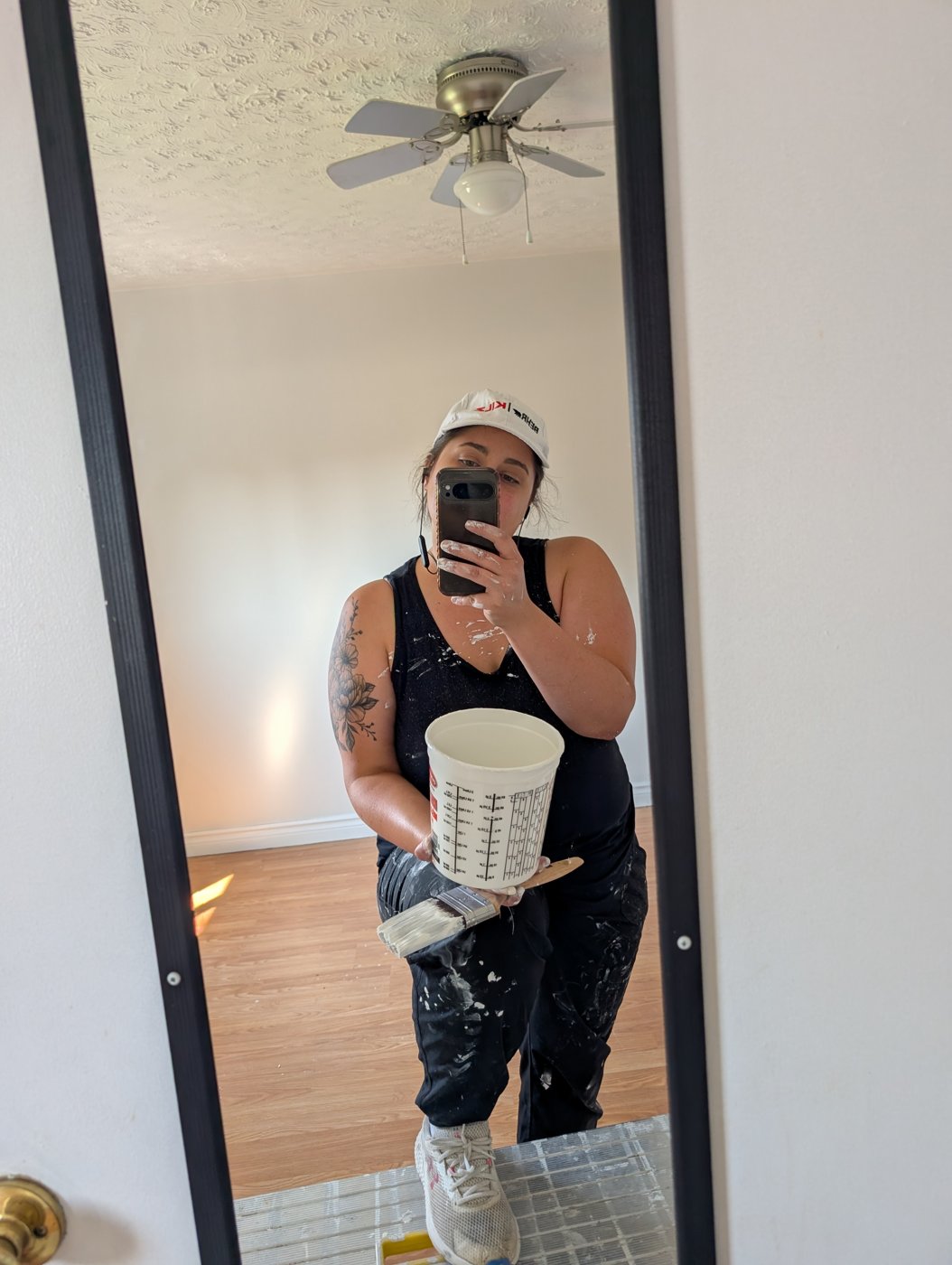 Cyan Goulet in paint splattered work clothes holding a paint cup and brush on an interior painting job