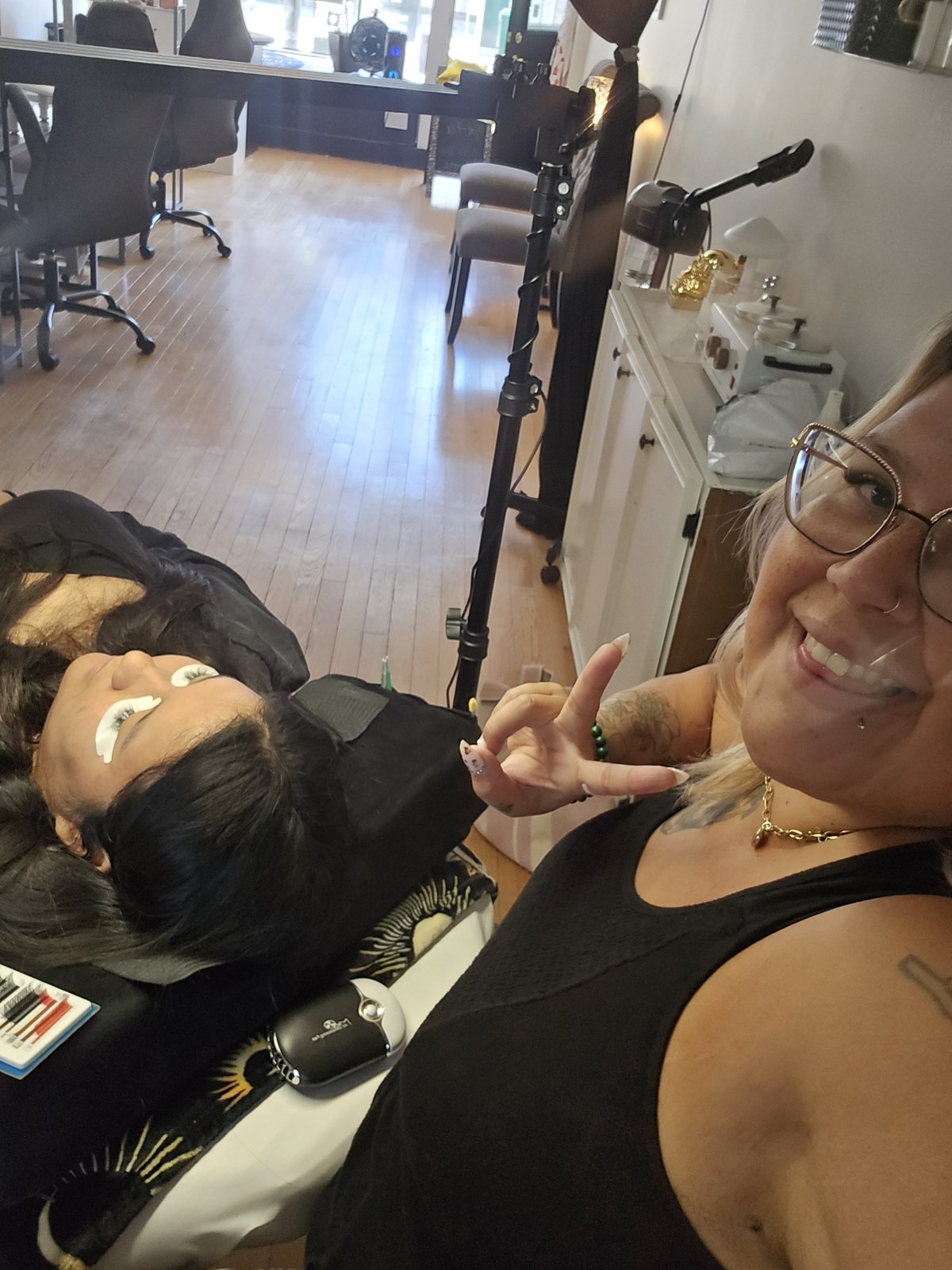 Kelly McKenzie smiling in her studio beside a client resting during a lash appointment